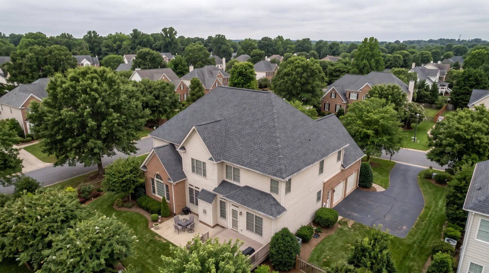 The same house from the same drone position after replacement, with a new charcoal architectural shingle roof on every slope and the patio cleared